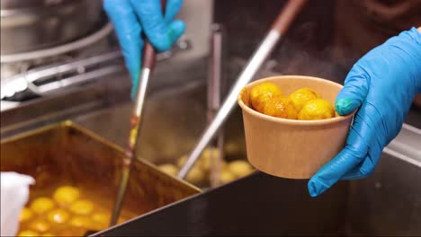 gloved hands serving meatballs into a bowl