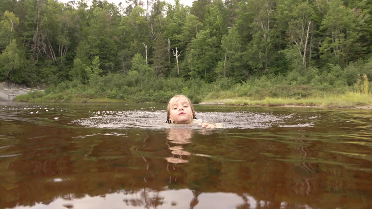 북부 온타리오 호수에서 카메라를 향해 수영하는 행복한 어린 소녀, 느린 동작