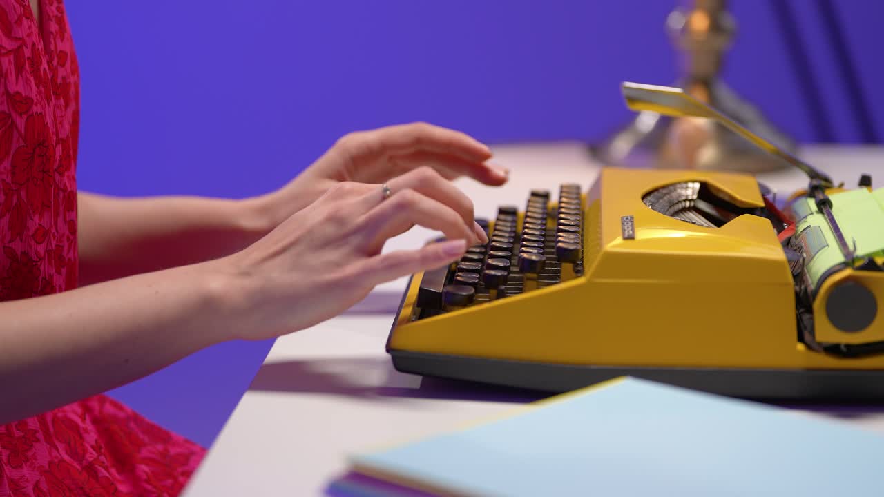 Macro shot of female hands typing on a yellow retro typewriter in a vibrant office. Colorful papers, soft lighting, and nostalgic atmosphere enhance this slow motion vintage scene