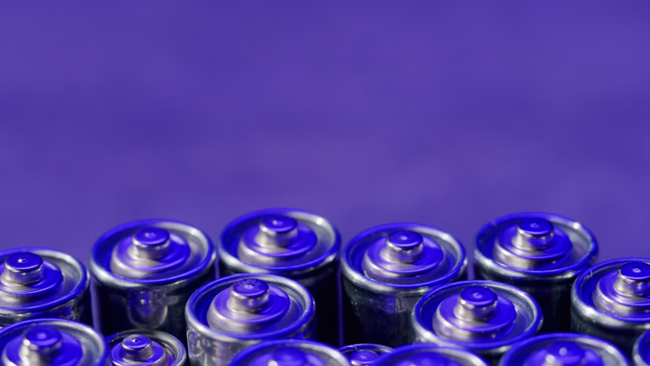 Silver batteries AA and AAA in neon light close-up. Double-A battery is a standard size single cell cylindrical dry battery. Batteries are common in portable electronic devices. An AA battery is composed of a single electrochemical cell that may be either a primary battery or a rechargeable battery.