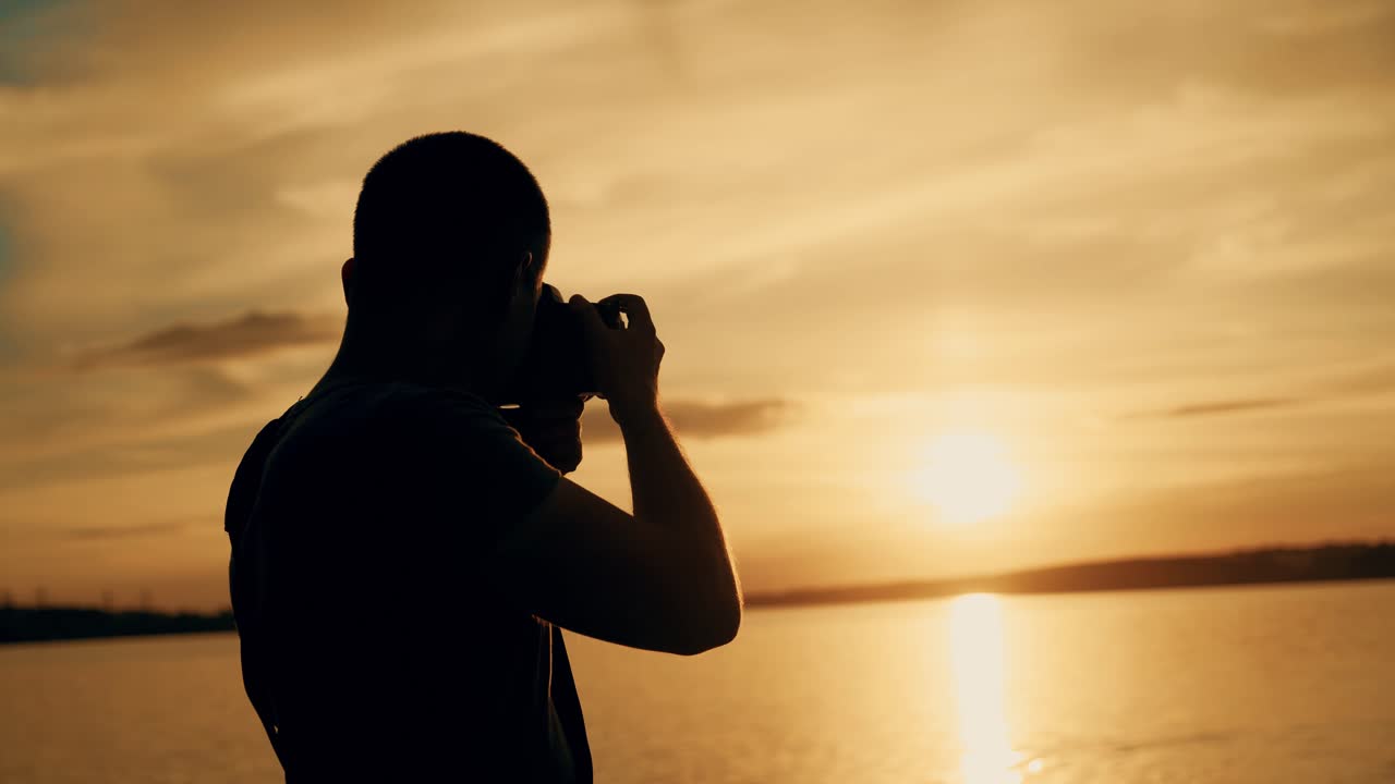 a man looks at the photos in the camera near the river at sunset. The guy chooses the best photos