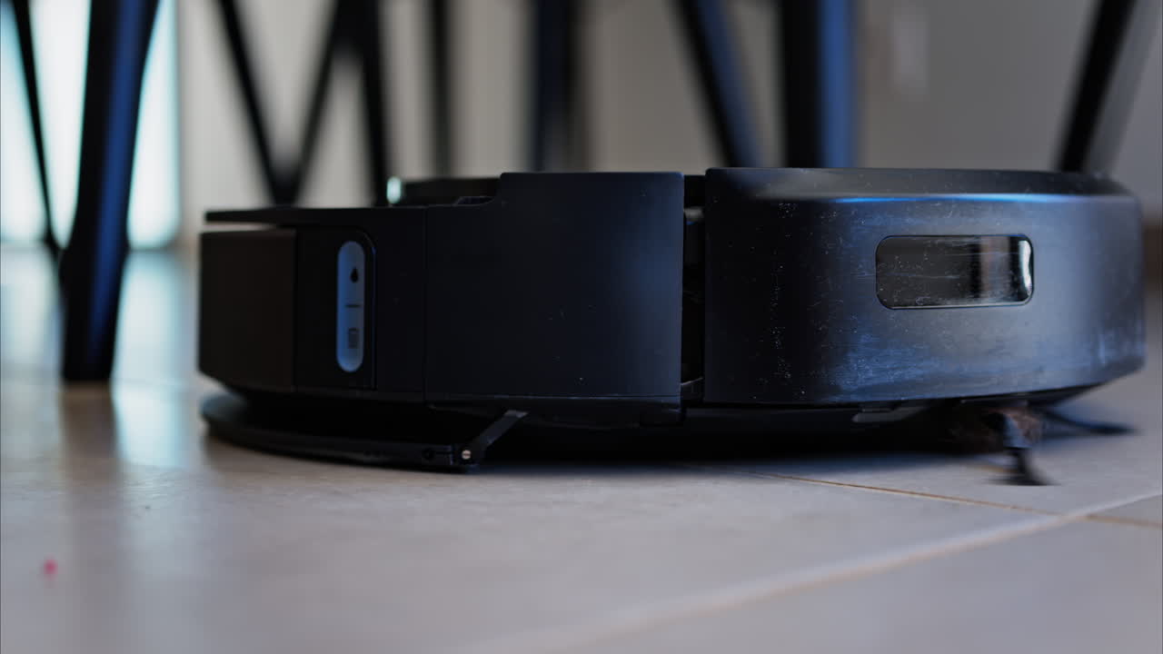 Close up of a small, black robot vacuum cleaning the house
