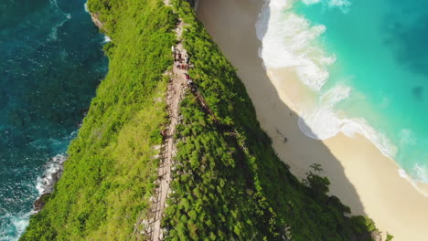 slow motion aerial of tourists hiking on steep forested cliffs of nusa penida