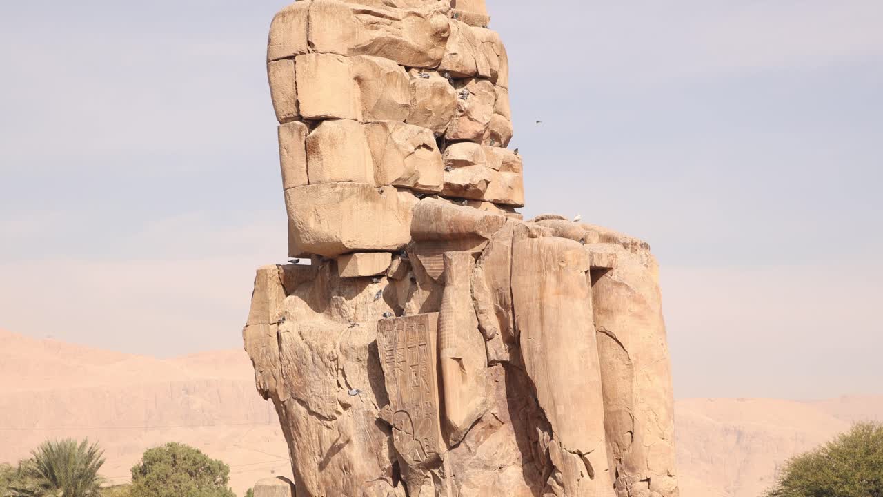 ruinas de la estatua gigante de faraón con montañas en el fondo en los colosos de memnon en luxor, egipto