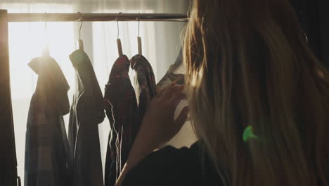 silhouette of a woman who chooses a shirt near the window. the setting sun illuminates the clothes beautifully