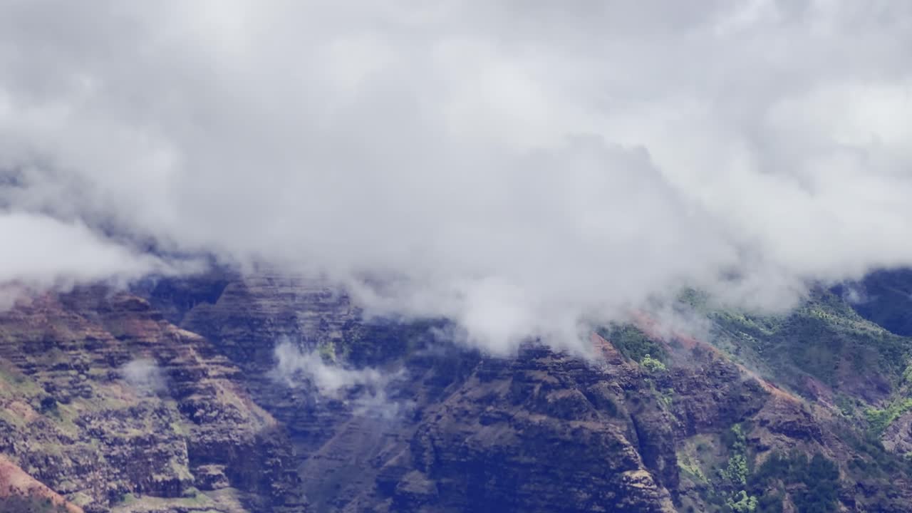 Cinematic long lens panning shot of thick clouds blanketing colorful Waimea Canyon on the island of Kaua'i, Hawai'i