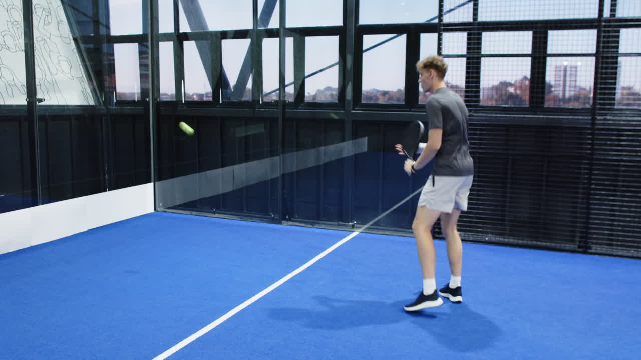 Young man playing padel tennis on blue indoor court, preparing to hit ball
