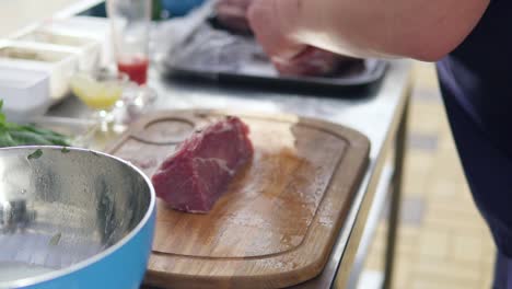 person's hands cutting a piece of raw meat using a butcher's knife on a wooden surface outside. barbeque preparation. shot in 4k