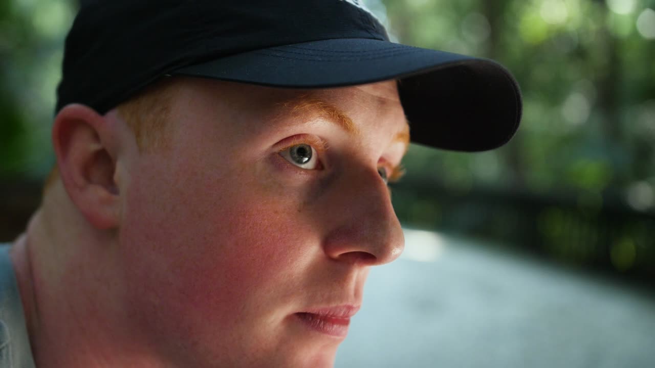 공원에 앉아서 주위를 둘러보고 있는 젊은 백인 남성의 클로즈업