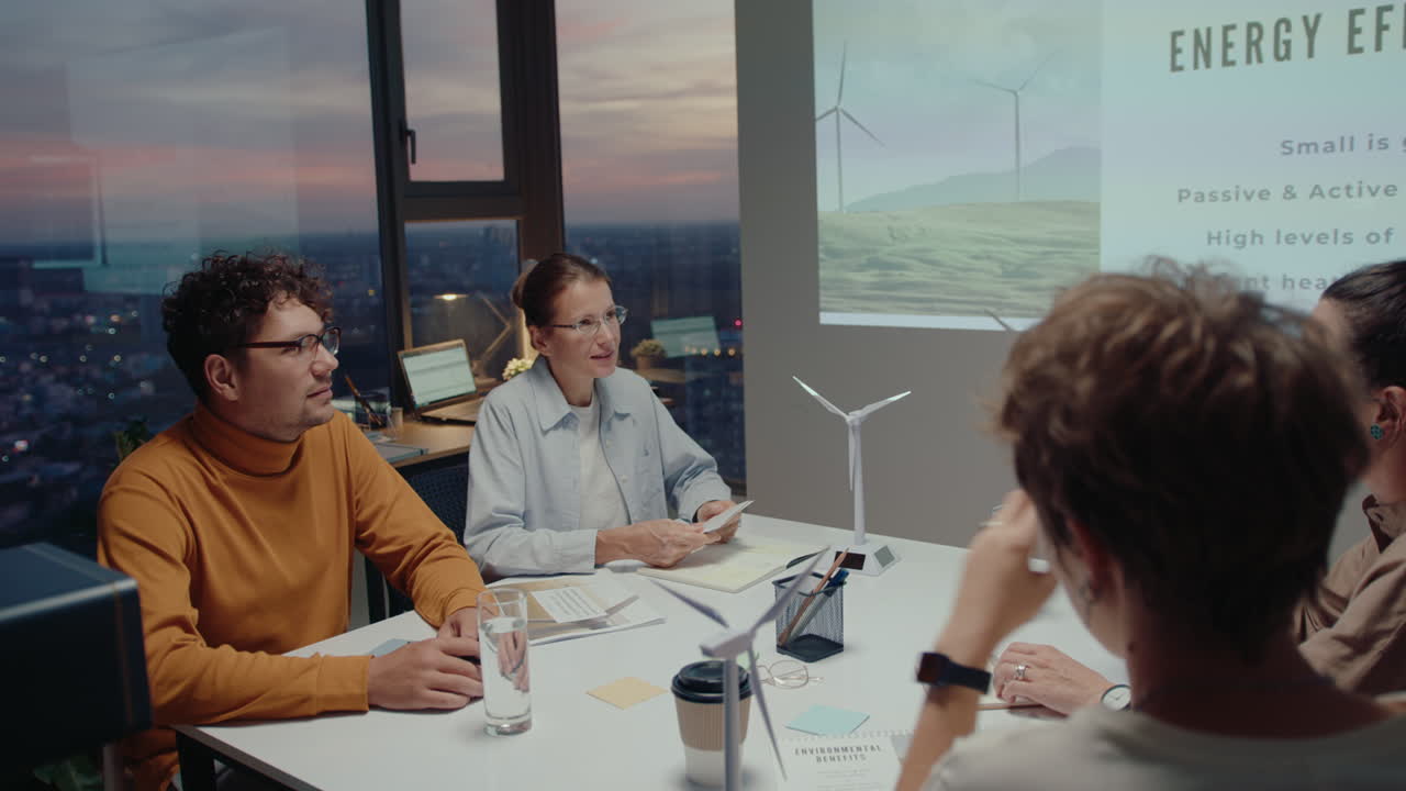 Team of business people watching presentation about sustainable energy and having discussion during office meeting in the evening