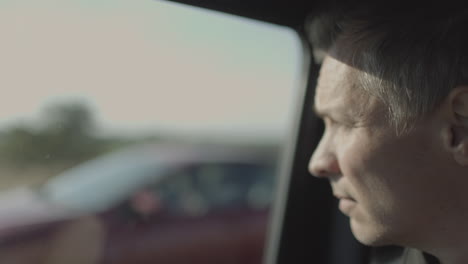 adult caucasian man staring out the passenger side of a car on the highway stares out the window as a red car goes past