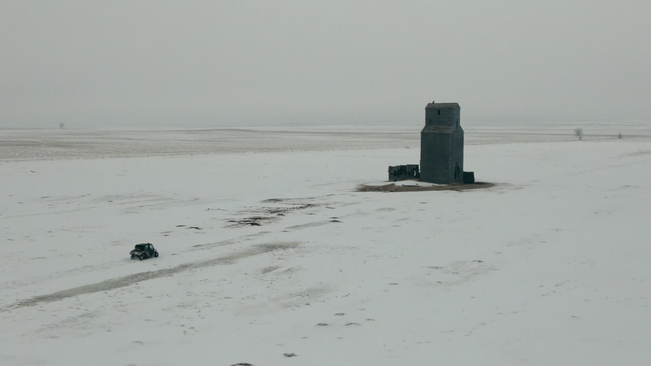 Aerial shot of UTV side by side approaching building on snowy prairie in winter, 4K