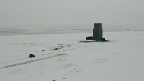 Aerial-shot-of-UTV-side-by-side-approaching-building-on-snowy-prairie-in-winter,-4K