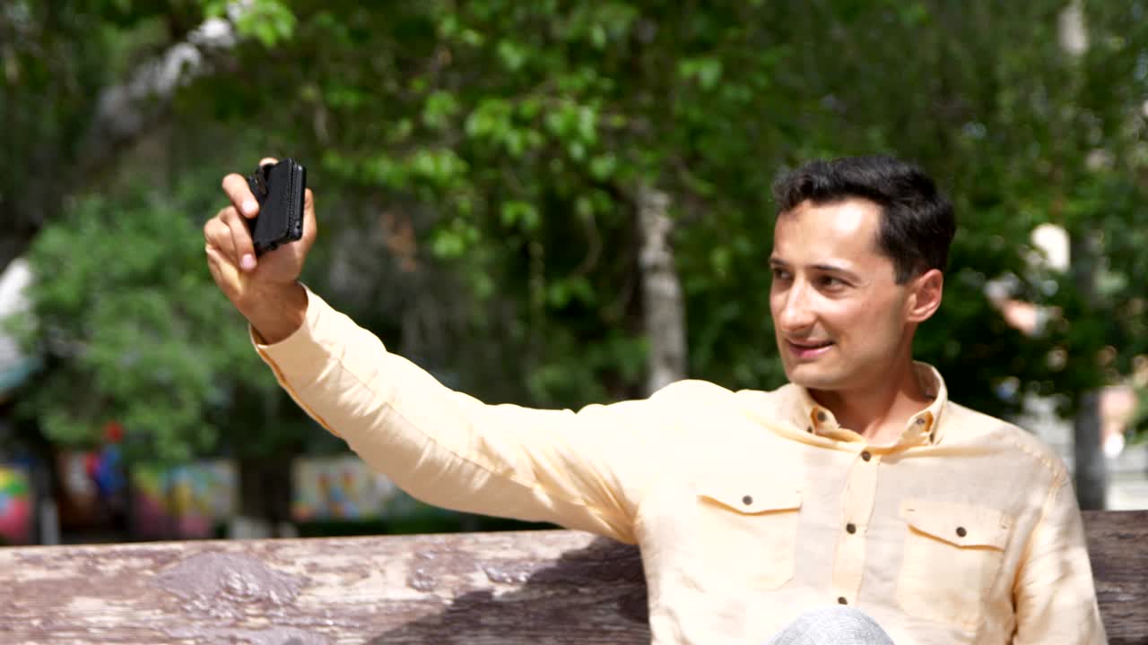 공원의 벤치에 앉아 전화로 셀피를 찍는 멋진 남자