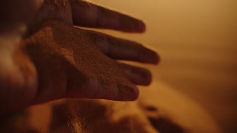 A close-up shot of a hand letting fine golden Sahara sand flow through the fingers, captured in warm evening light during sunset in the Moroccan desert