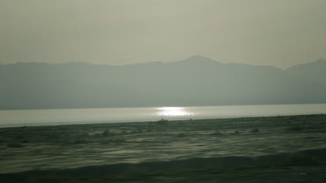 hazy mountains and lake with sun reflection
