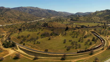 A-long-train-stretches-the-full-length-of-the-Tehachapi-Loop-spiral---slow-motion-aerial-view
