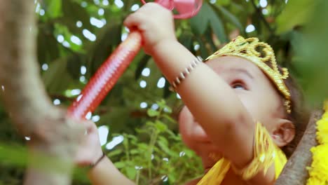 un bebé adorable vestido como el dios hindú Krishna con una linda expresión facial jugando en el árbol en Janmashtami
