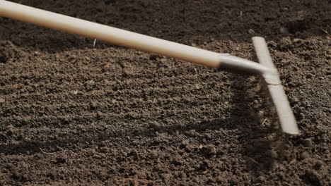 Farmer-leveling-the-ground-with-a-rake-in-the-garden,-preparing-for-planting.-Side-view