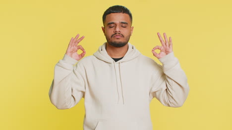 indian man meditating breathes deeply with mudra yoga gesture, eyes closed, taking a break, relax