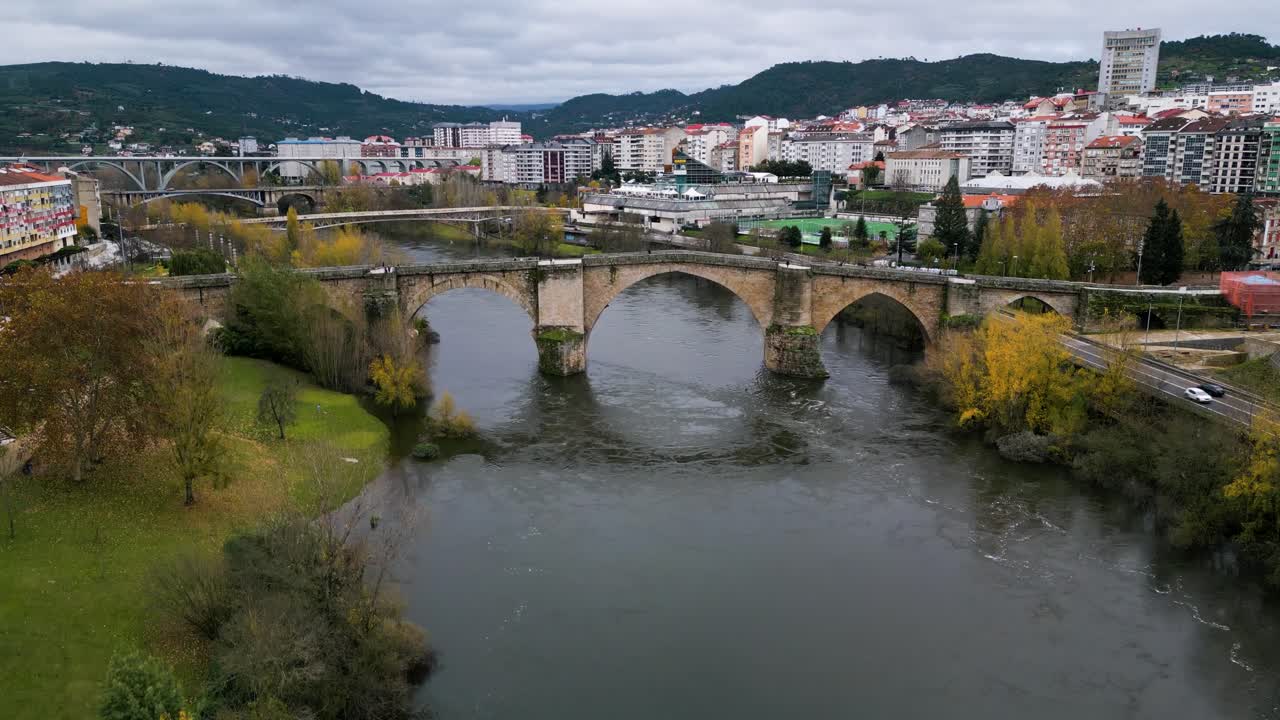 Drone descends to river with reflection of Ourense Roman Bridge on Mi&ntilde;o River in Ourense, Galicia, Spain