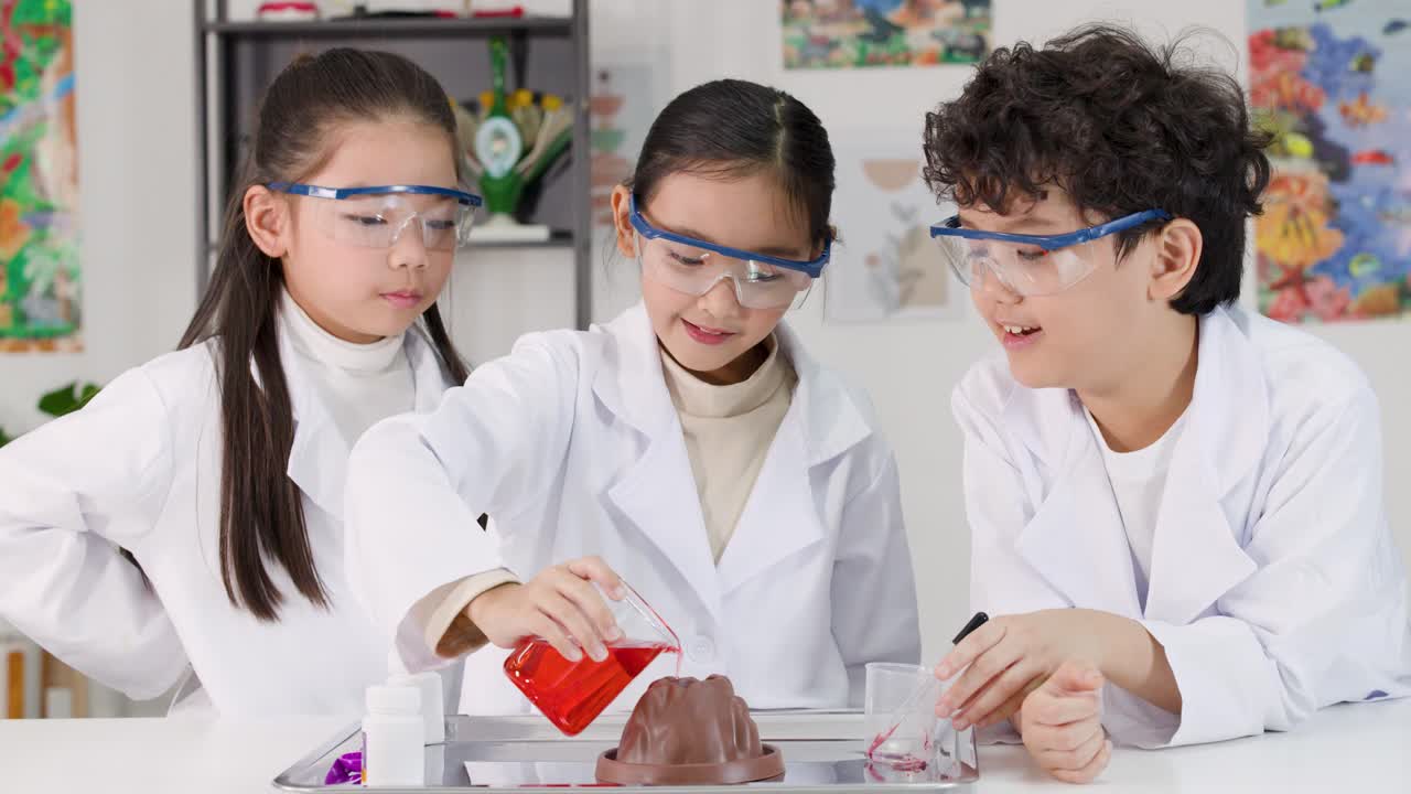 白衣と安全ゴーグルを着用した3人の学生が屋内で行う化学反応火山実験。