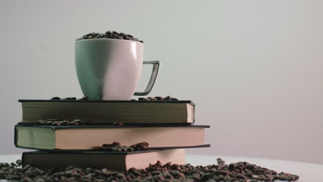 Rotating-display-with-a-stack-of-books-and-a-coffee-mug,-with-brown-roasted-coffee-beans