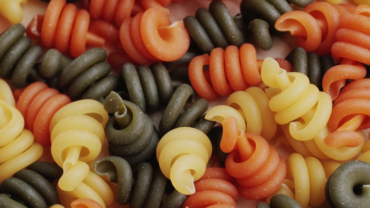 Primo piano di pasta a spirale tricolore cruda che si allontana lentamente