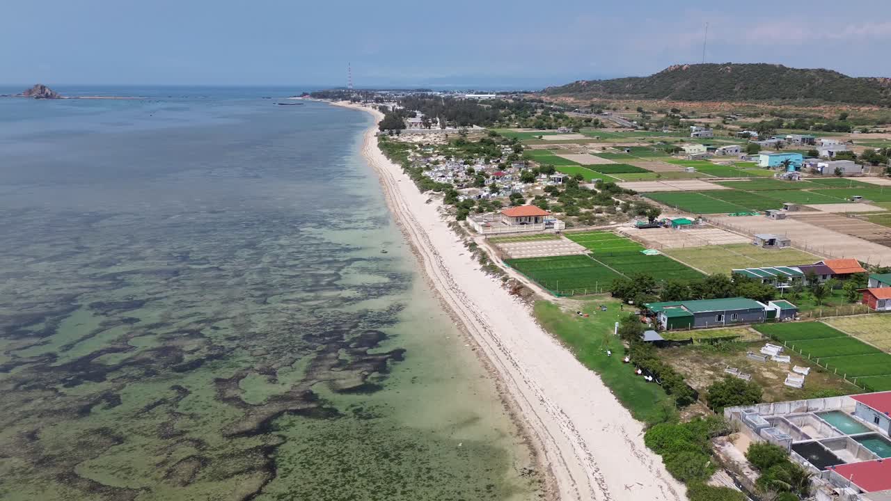 4K drone pulls back while panning left, revealing the calm sea and endless horizon near Phan Rang, Vietnam. Peaceful coastal view in daylight