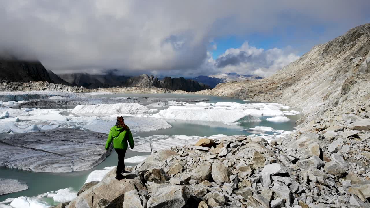 sobrevuelo aéreo sobre un excursionista junto al lago glaciar lleno de icebergs derretidos en partes remotas de los alpes suizos en un día soleado