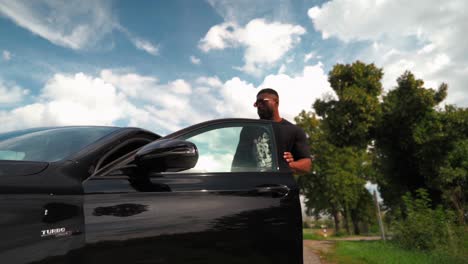 African-Sporty-Man-Getting-Out-of-Modern-Black-Car-and-Walking-Towards-Trunk-on-Summer-day