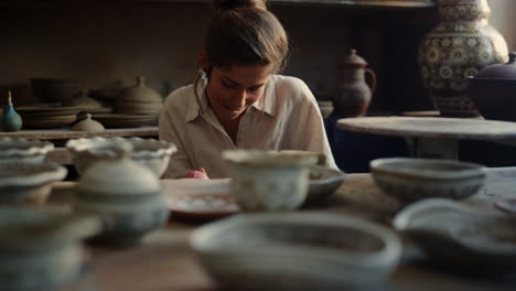 excited ceramist drawing ornament in studio. woman doing handcraft in workshop