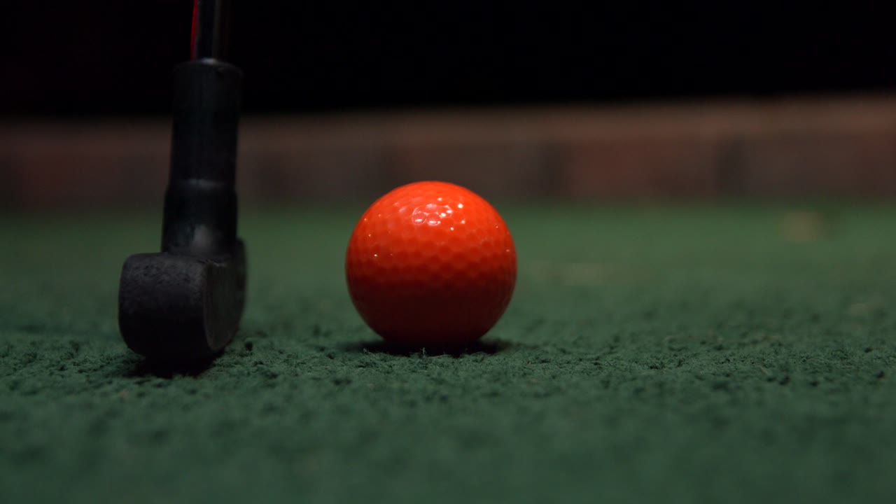 Primissimo piano di un putter da minigolf che colpisce una pallina da golf arancione.