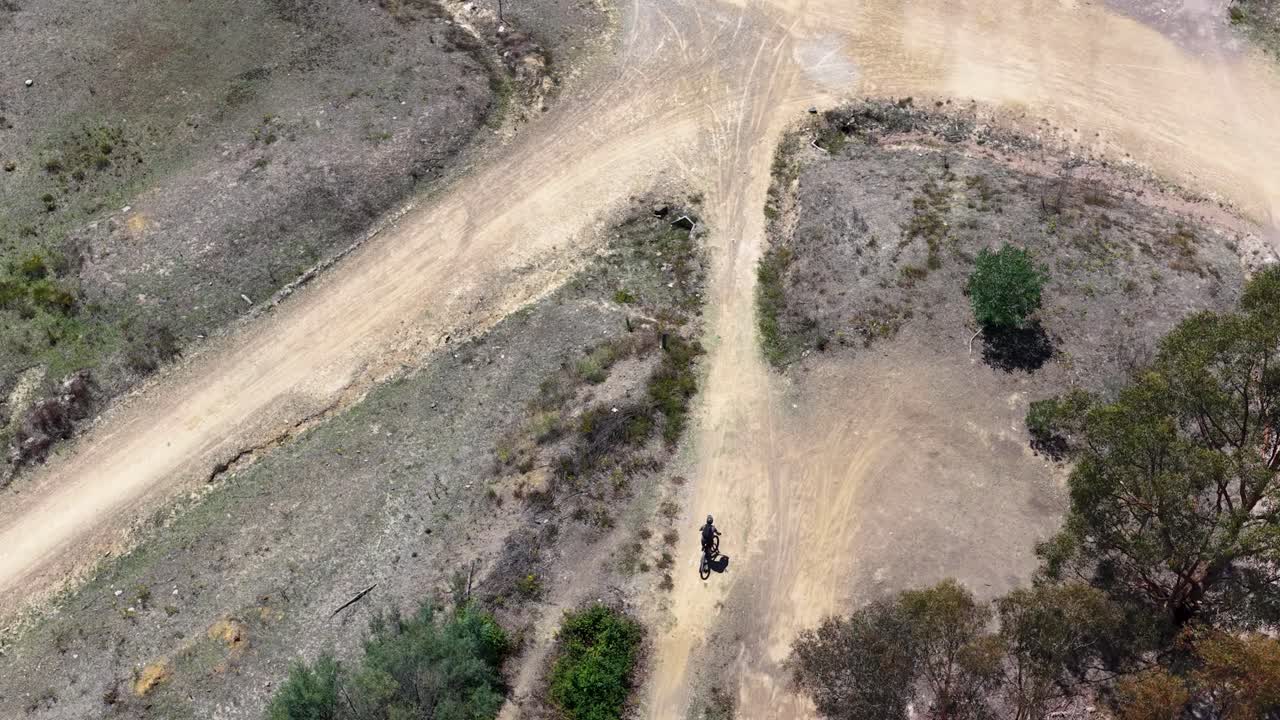 Ripresa aerea dall'alto con drone che segue un ciclista solitario mentre percorre un sentiero sterrato attraverso il bush australiano