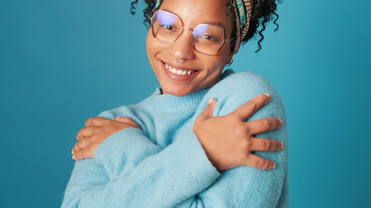 Mujer joven y feliz abrazándose a sí misma y sonriendo en el estudio