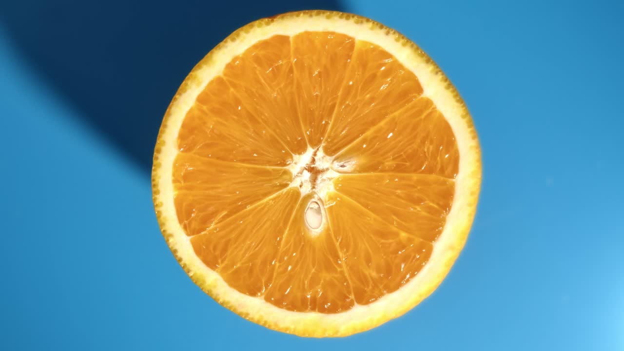 Rotazione di una metà di arancia fresca e appetitosa, con texture di semi e buccia, vista dall'alto, isolata su sfondo blu