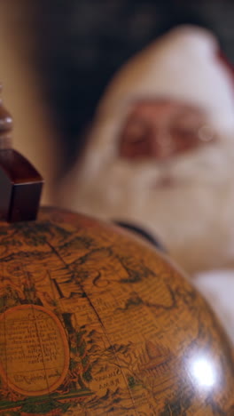 santa claus with globe. big round globe and santa looking at it through the magnifying glass. close-up. vertical video