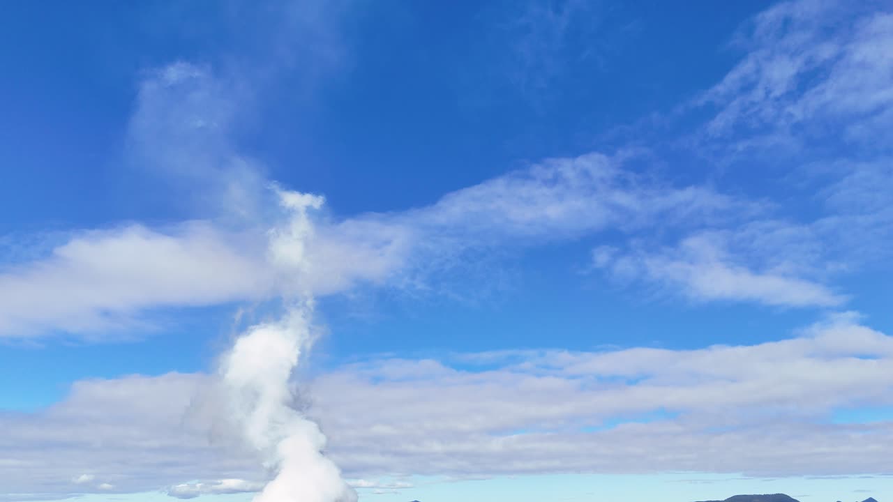 Drone captures smoke stack releasing steam against a vibrant blue sky, highlighting air pollution and climate change concerns
