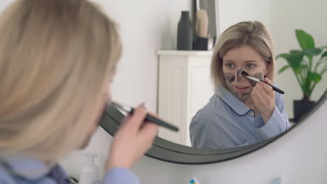 female applying facial mask looking to the mirror