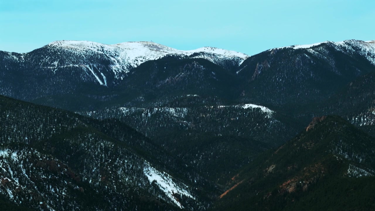 Pemandangan udara drone Pegunungan Cheyenne yang tertutup salju di Front Range Pegunungan Rocky, Colorado Springs, Colorado. Pagi hari musim dingin-semi dengan langit biru berawan di selatan Denver, Colorado, dengan gerakan melingkar ke kanan.
