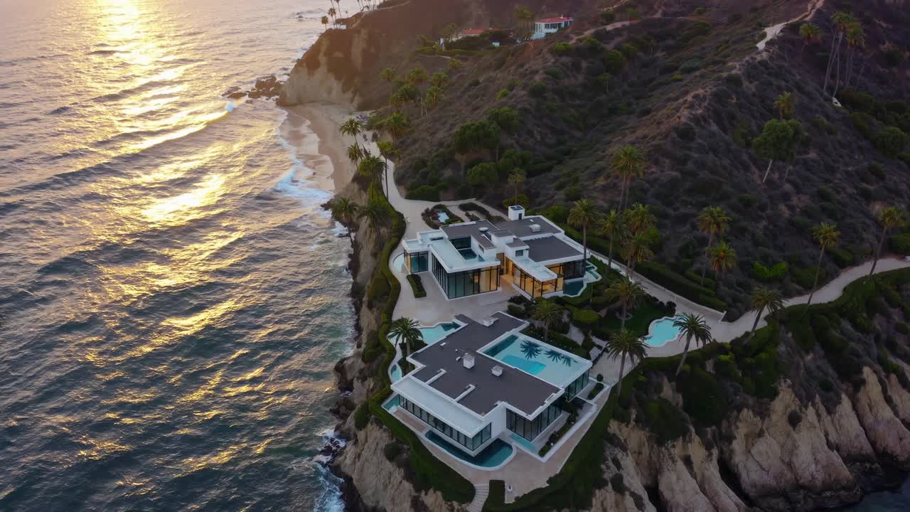 Golden hour illuminating shimmering ocean waves near luxurious cliffside residence, featuring infinity pool and swaying palms overlooking dramatic California coastal landscape
