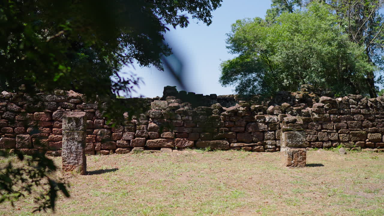 Sunlight illuminates the ruins of San Ignacio Miní, showcasing crumbling walls of red stones, remnants of a Jesuit reduction in Misiones, Argentina, a reminder of a bygone era, slow motion shot