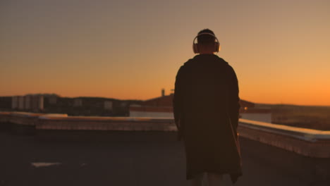 a man walks on the roof at sunset with headphones looking at the city from the height of a skyscraper at sunset. relax while listening to music. enjoy a beautiful view of the city at sunset from the roof with headphones