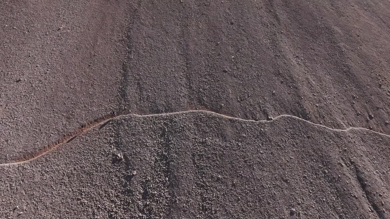 Drone rotating slowly filming two persons walking on a mountain path in 4k