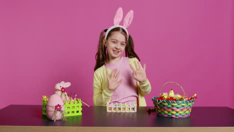 joyful child putting bunny ears on her head and waving at camera