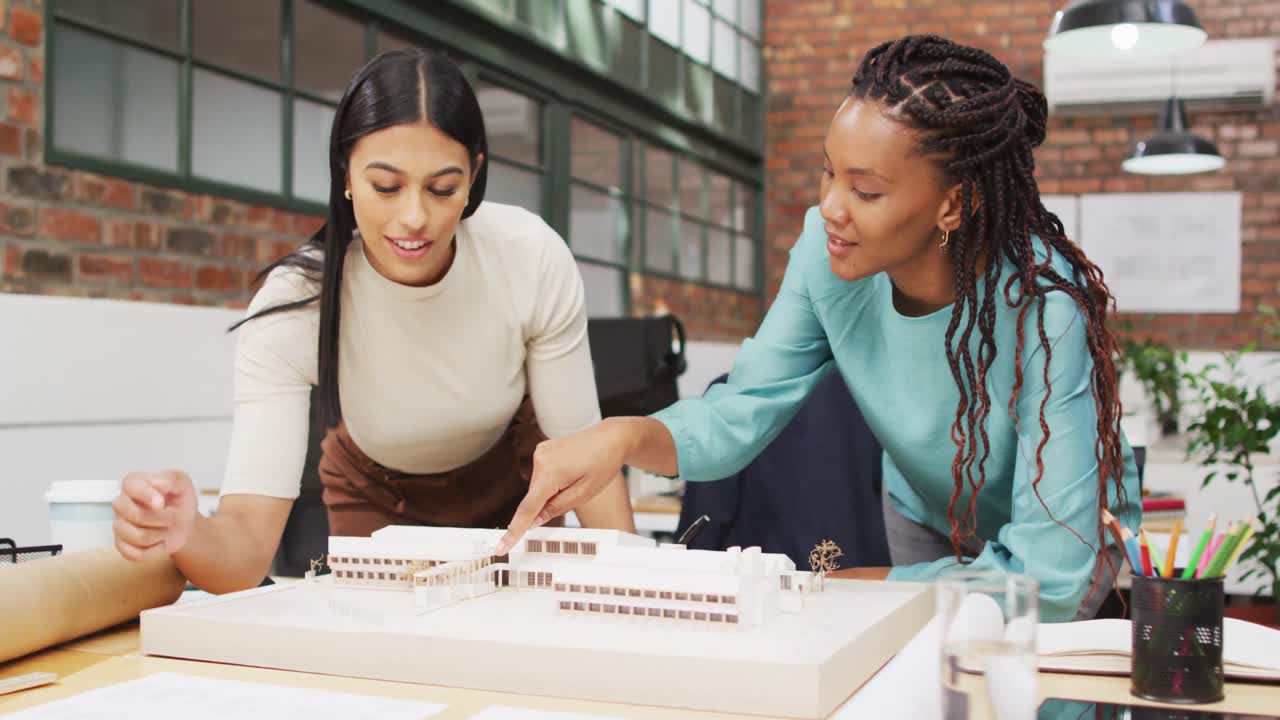 Happy diverse female architects looking at architectural models at office