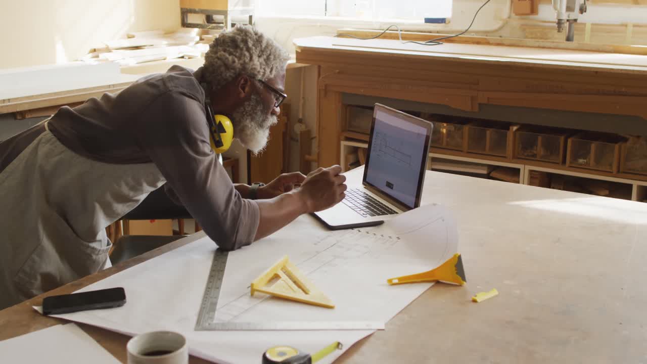 carpintero afroamericano usando una computadora portátil en una carpintería