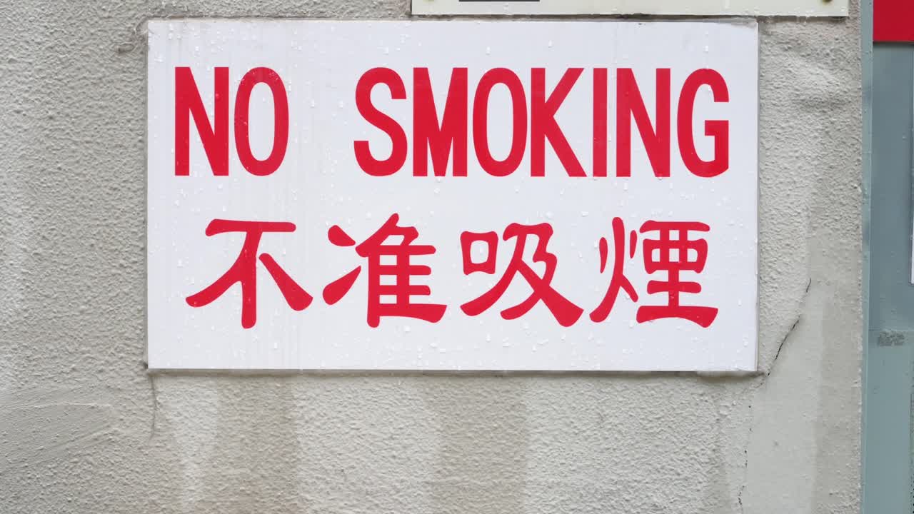 A red-lettered "No Smoking" sign in English and Chinese is displayed on a wall in Hong Kong, China, prohibiting smoking in public.