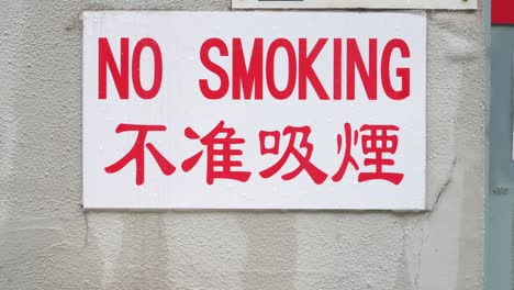 a red-lettered "no smoking" sign in english and chinese is displayed on a wall in hong kong, china, prohibiting smoking in public.