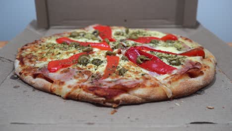manos tomando rebanadas de una deliciosa pizza con jamón, queso, pimientos rojos y aceitunas